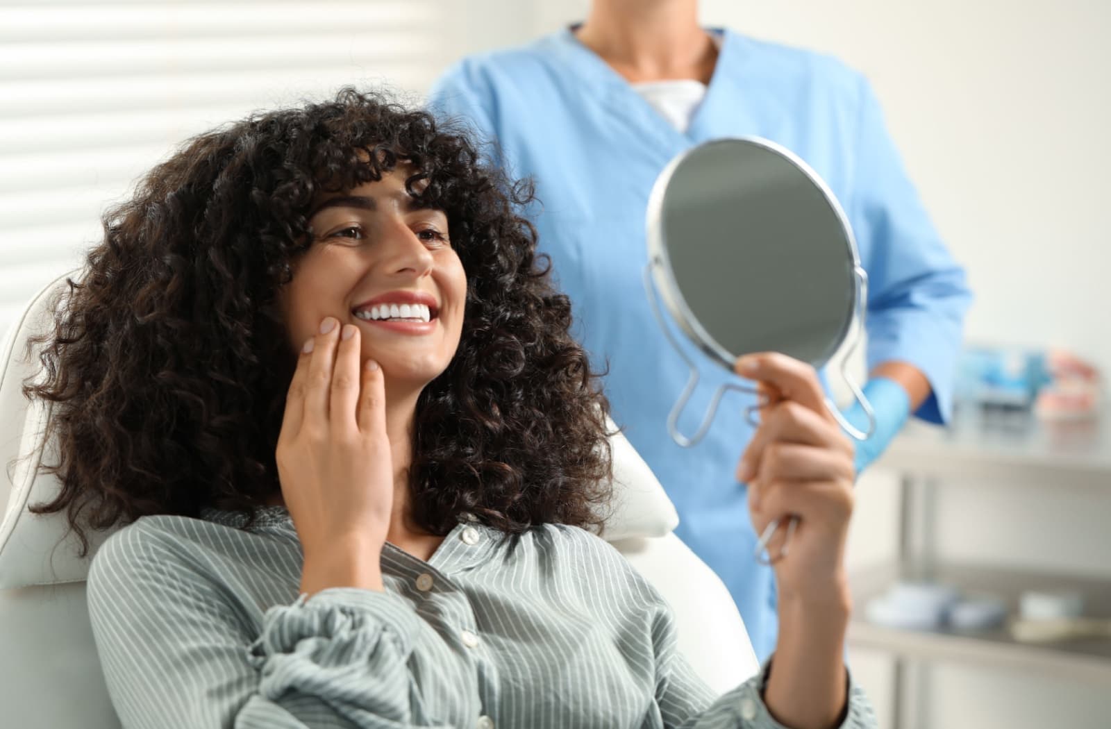 A person inspects their new dental implants using a mirror at the dentist's office.