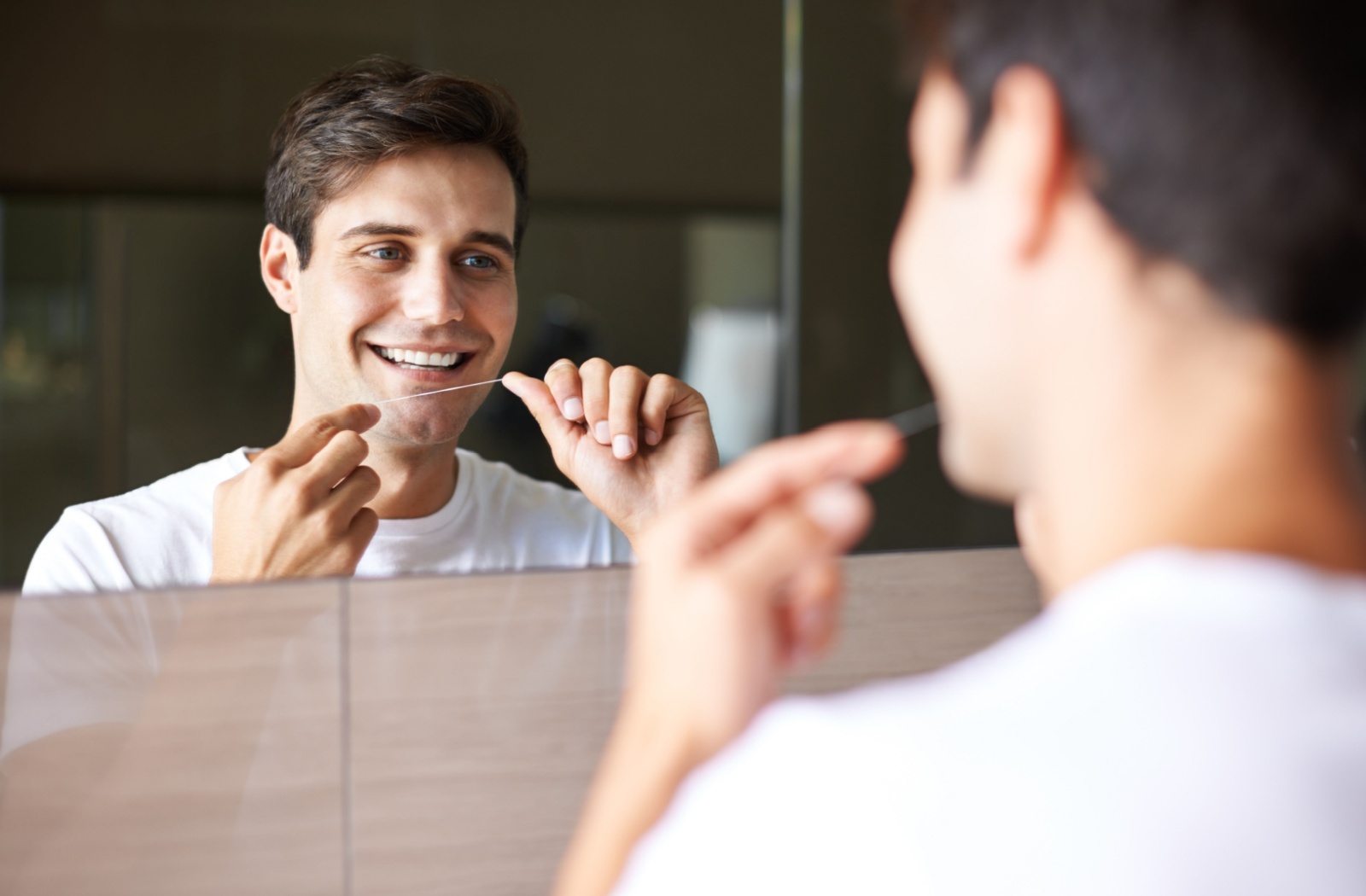 Young person flossing while looking at their reflection in the mirror.