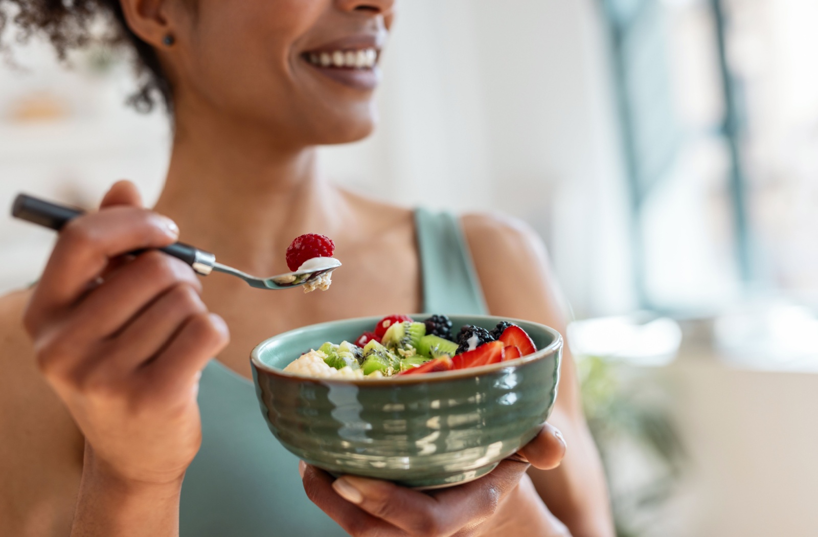  A person smiling, eating a bowl of fruit.