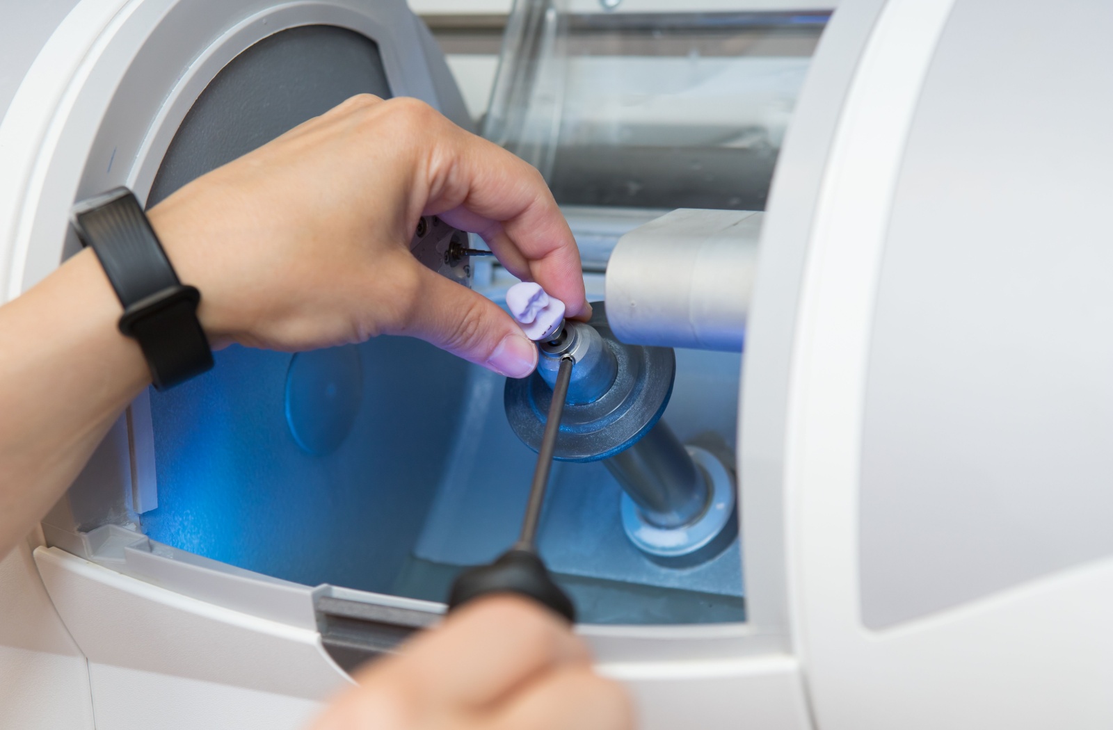 A dental crown is finished being milled, and a professional removes the piece.