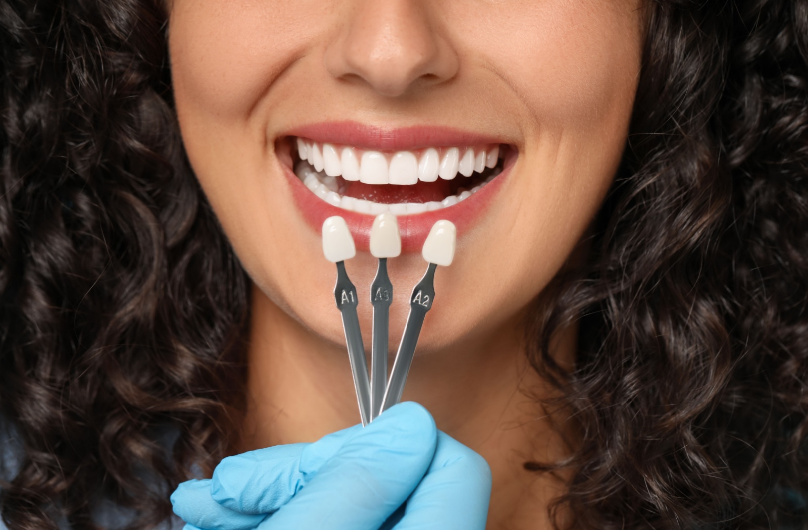 A woman sitting in a dental chair looking into a handheld mirror, admiring her smile after professional teeth whitening and dental crown services.